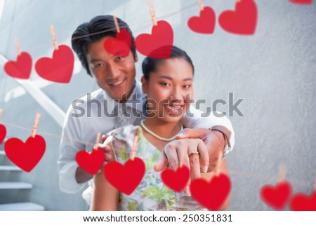 Couple showing engagement ring on womans finger against hearts hanging on a line