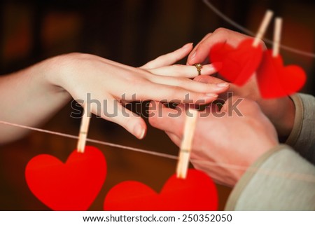 Close up on man putting on ring during marriage proposal against hearts hanging on a line