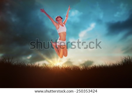 Gorgeous fit blonde jumping with arms out against blue sky over grass