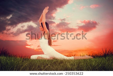Sporty woman with joined hands over head at a fitness studio against red sky over grass