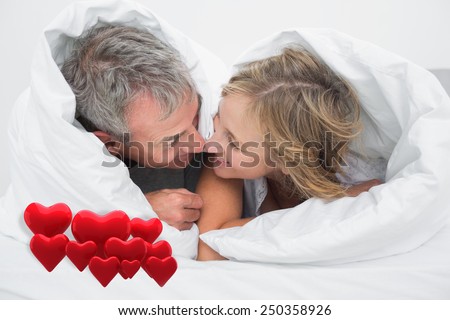 Loving middle aged couple under the duvet against love hearts