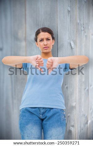 Pretty brunette giving thumbs down against bleached wooden planks background