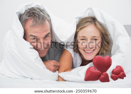 Happy middle aged couple under the duvet against love hearts
