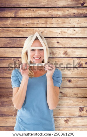 Happy blonde holding house outline over face against wooden planks