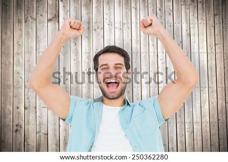 Happy casual man cheering at camera against wooden planks background