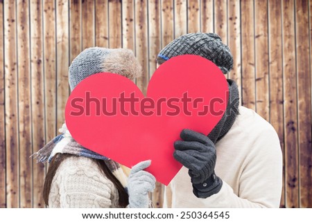 Attractive young couple in warm clothes holding red heart against wooden planks