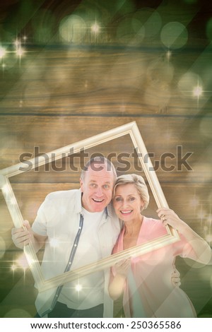 Older couple smiling at camera through picture frame against light design shimmering on green