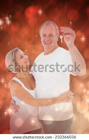 Mature couple smiling at camera with new house key against light design shimmering on red