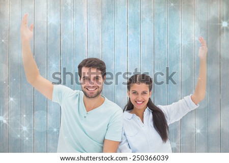 Cute couple sitting with arms raised against shimmering light design on grey