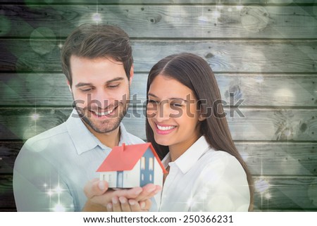 Attractive young couple holding a model house against light design shimmering on green