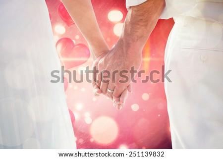 Bride and groom holding hands close up against valentines heart design