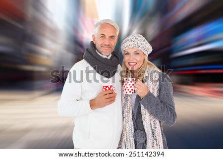 Happy couple in winter fashion holding mugs against blurry new york street
