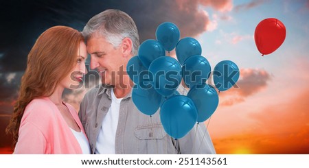 Casual couple hugging and smiling against orange and blue sky with clouds