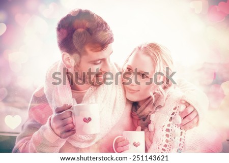 Loving young couple in winter clothing with coffee cups against cabin window