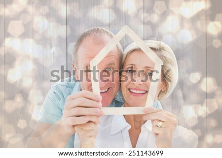 Happy older couple holding house shape against light glowing dots design pattern