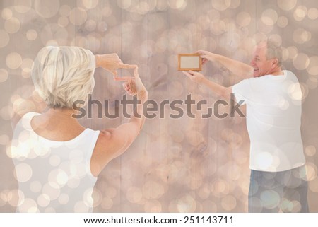 Mature couple hanging up picture frame against light glowing dots design pattern