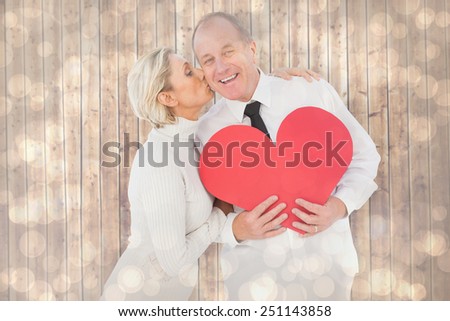 Older affectionate couple holding red heart shape against light glowing dots design pattern