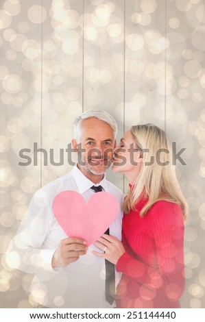 Handsome man holding paper heart getting a kiss from wife against light glowing dots design pattern