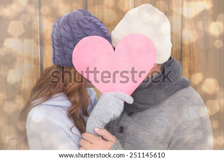 Couple in warm clothing holding heart against light glowing dots design pattern
