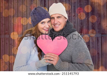 Happy couple in warm clothing holding heart against close up of christmas lights