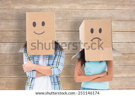 Young couple wearing sad face boxes over head against wooden surface with planks
