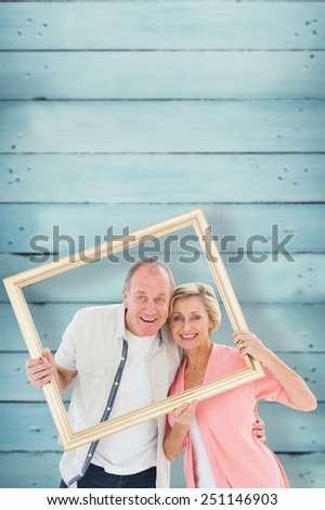 Older couple smiling at camera through picture frame against wooden planks