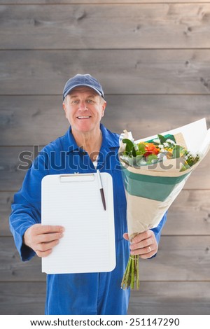 Happy flower delivery man showing clipboard against wooden planks