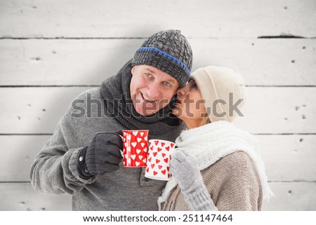 Happy mature couple in winter clothes holding mugs against white wood