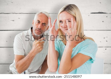 Unhappy couple sitting on chairs having an argument against white wood