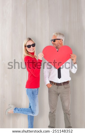 Cool couple holding a red heart together against bleached wooden planks background