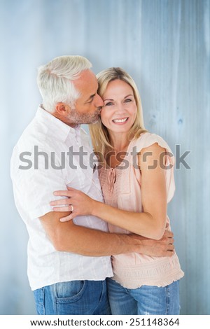 Affectionate man kissing his wife on the cheek against bleached wooden planks background