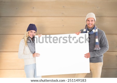 Attractive couple in winter fashion showing poster against bleached wooden planks background