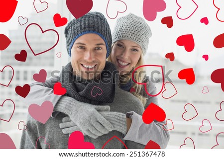 Cute couple in warm clothing hugging smiling at camera against valentines heart design