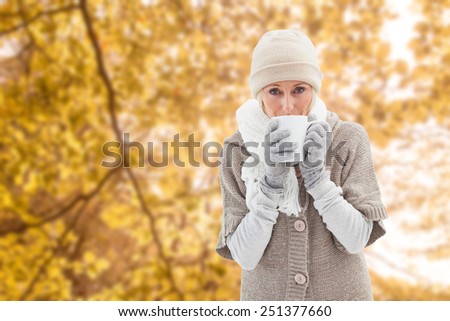 Woman in warm clothing holding mugs against tranquil autumn scene in forest