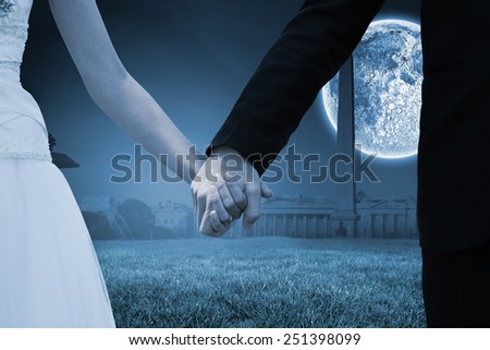 Mid section of newlywed couple holding hands in park against bright moon over paris