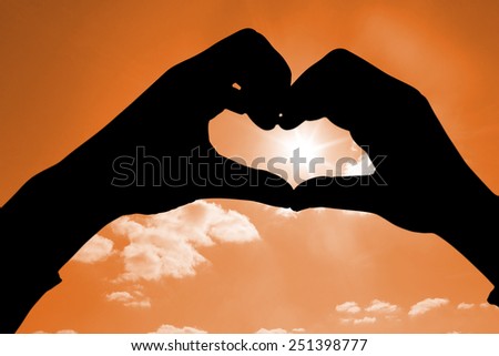 Woman making heart shape with hands against cloudy sky with sunshine