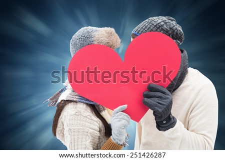 Attractive young couple in warm clothes holding red heart against blue abstract light spot design