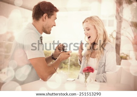 Man proposing marriage to his shocked blonde girlfriend on the cafe terrace on sunny day