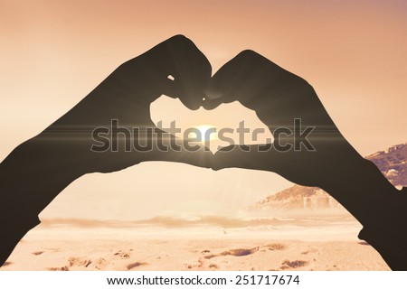 Woman making heart shape with hands against beautiful beach and blue sky