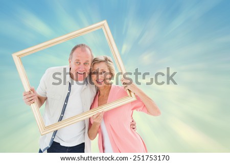 Older couple smiling at camera through picture frame against blue abstract light spot design