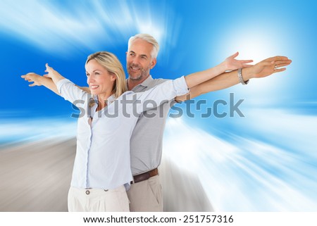 Happy couple standing with arms outstretched against large rock overlooking blue sky