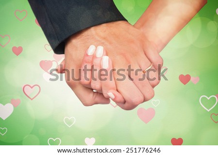 Newlyweds holding hands close up against love heart pattern