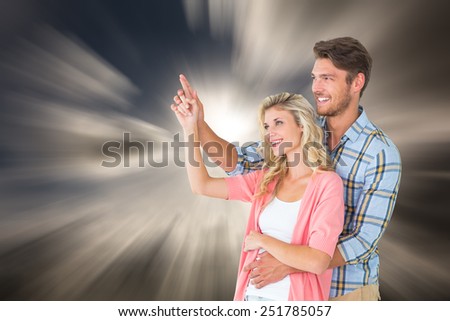 Attractive young couple embracing and pointing against dark sky with white clouds