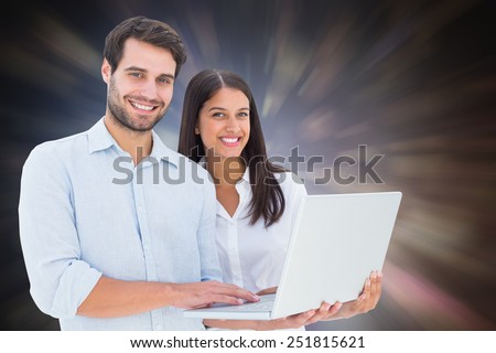Attractive young couple holding their laptop against dark abstract light spot design