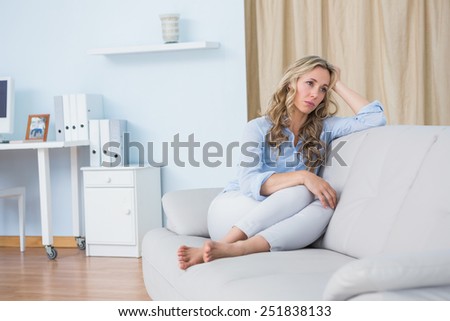 Blonde woman sitting on couch thinking at home in the living room