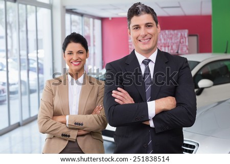 Smiling colleagues standing with arms crossed at new car showroom