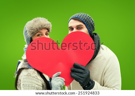 Attractive young couple in warm clothes holding red heart against green vignette