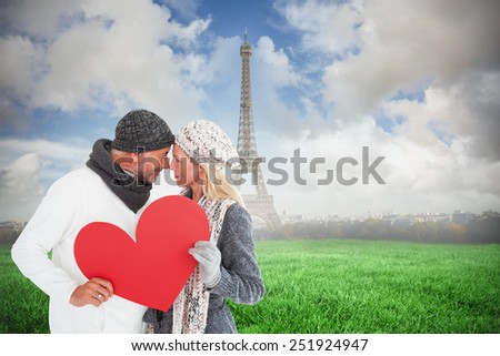 Smiling couple in winter fashion posing with heart shape against eiffel tower
