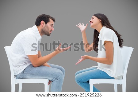 Couple sitting on chairs arguing against grey