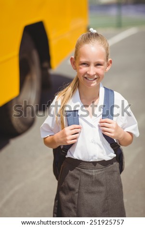 Cute pupil smiling at camera by the school bus outside the elementary school
